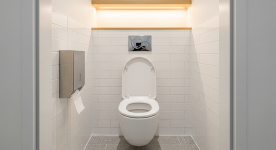 Bright modern toilet cubicle with white subway tiles and seat cover dispenser